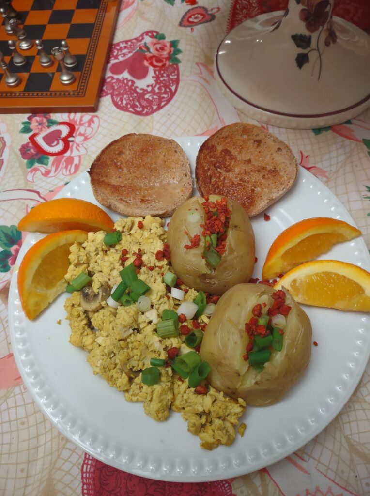 Plate with scrambled tofu, two baked potatoes, and an English muffin and orange slices