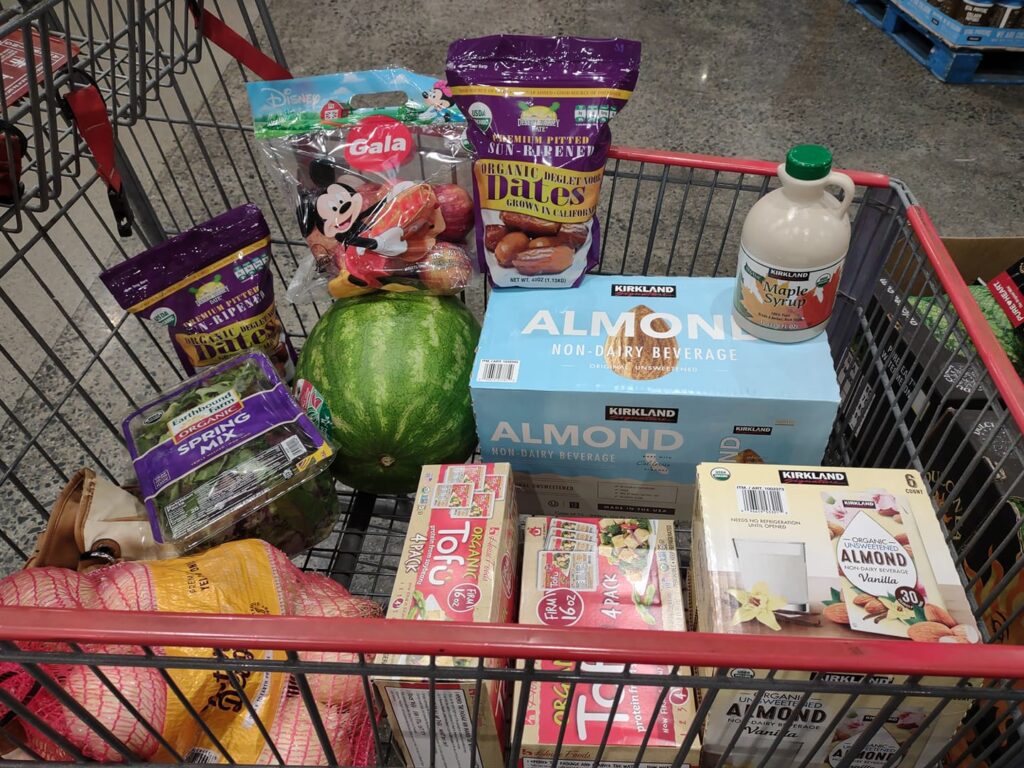 My cart at Costco with tofu, dates, watermelon, unsweetened almond milk and vanilla almond milk, salad pack, maple syrup, onions, apples