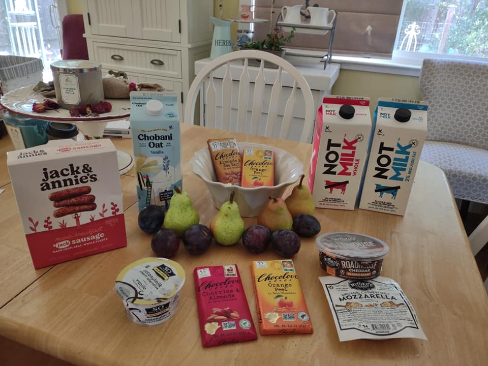 Sprouts shopping trip on my kitchen table: Not Milk, Chobani Oatmilk, Chocolove Bars, Miyoko's Cheeses, pears, plums, So Delicious yogurt
