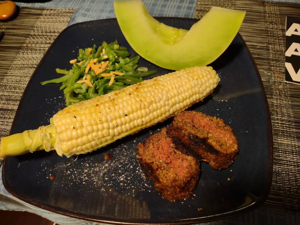 plate with vegan steak, honeydew melon and corn and green beans